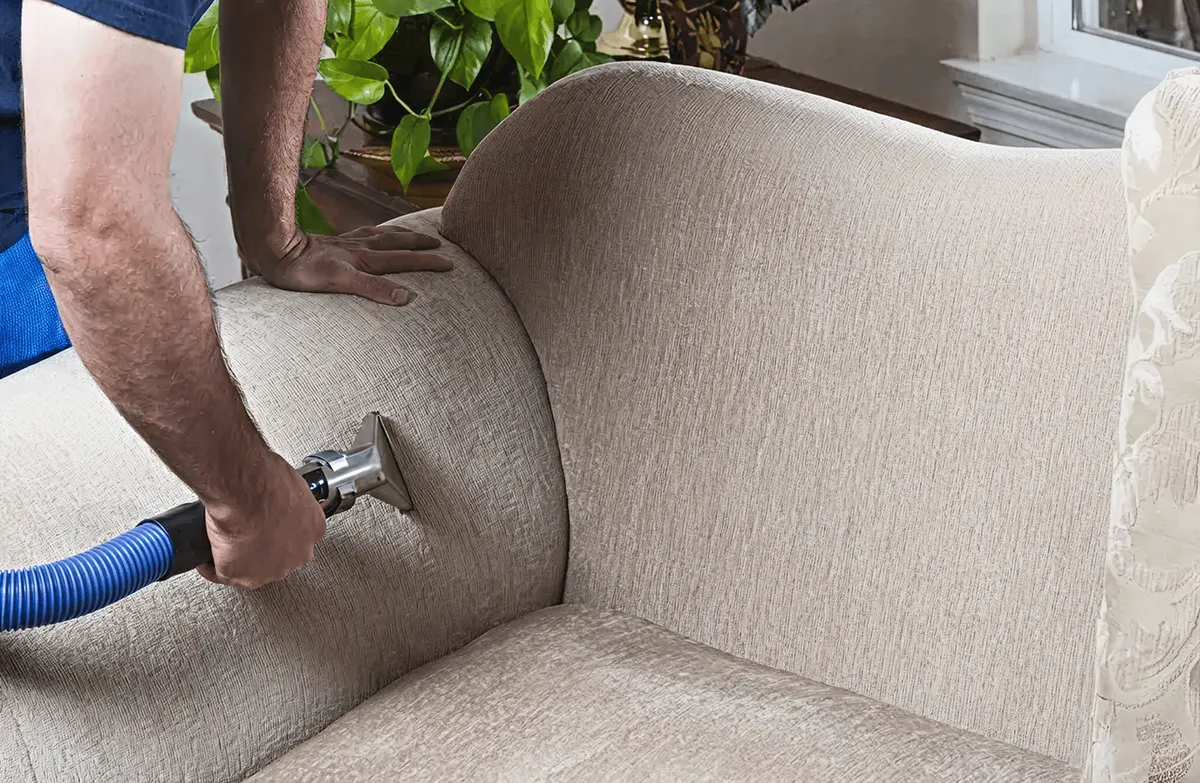 Professional upholstery cleaner deep-cleaning a fabric sofa with a handheld extraction tool and hose, Columbia, MO.